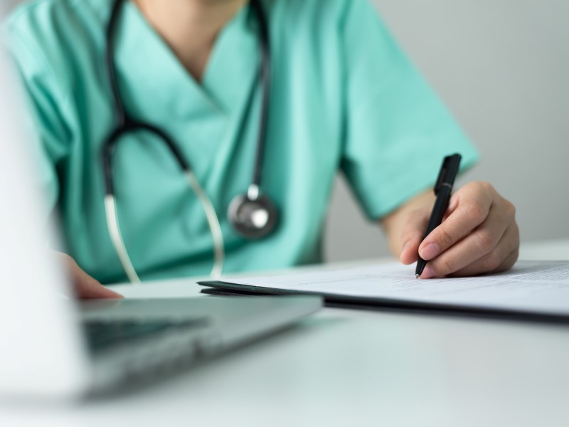 Nurse filling out information on paper with pen, also on laptop