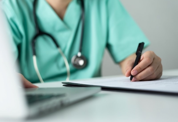 Nurse filling out information on paper with pen, also on laptop